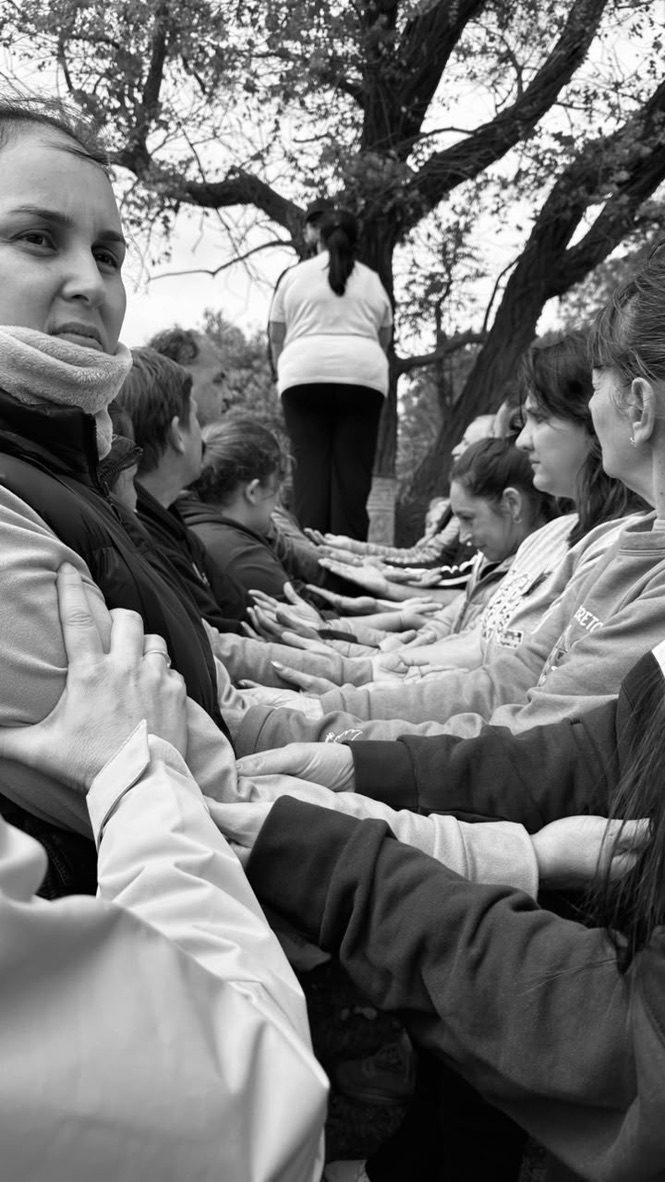 En blanco y negro, dos filas de estudiantes extienden los brazos para recibir a una compañera que se deja caer desde un tronco