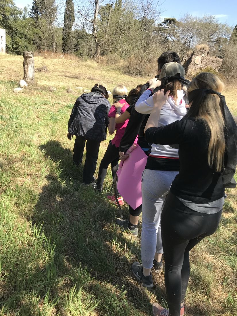 Estudiantes con los ojos vendados caminan en fila por el campo, con la mano en el hombro del compañero